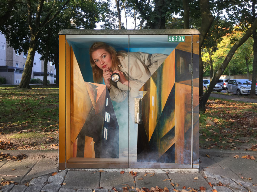 Künstlerisch umgestalteter Stromkasten. Zu sehen ist eine junge Frau die in einer Hand eine Taschenlampe hält, und hinter einem Kunstwerk hervorschaut.
