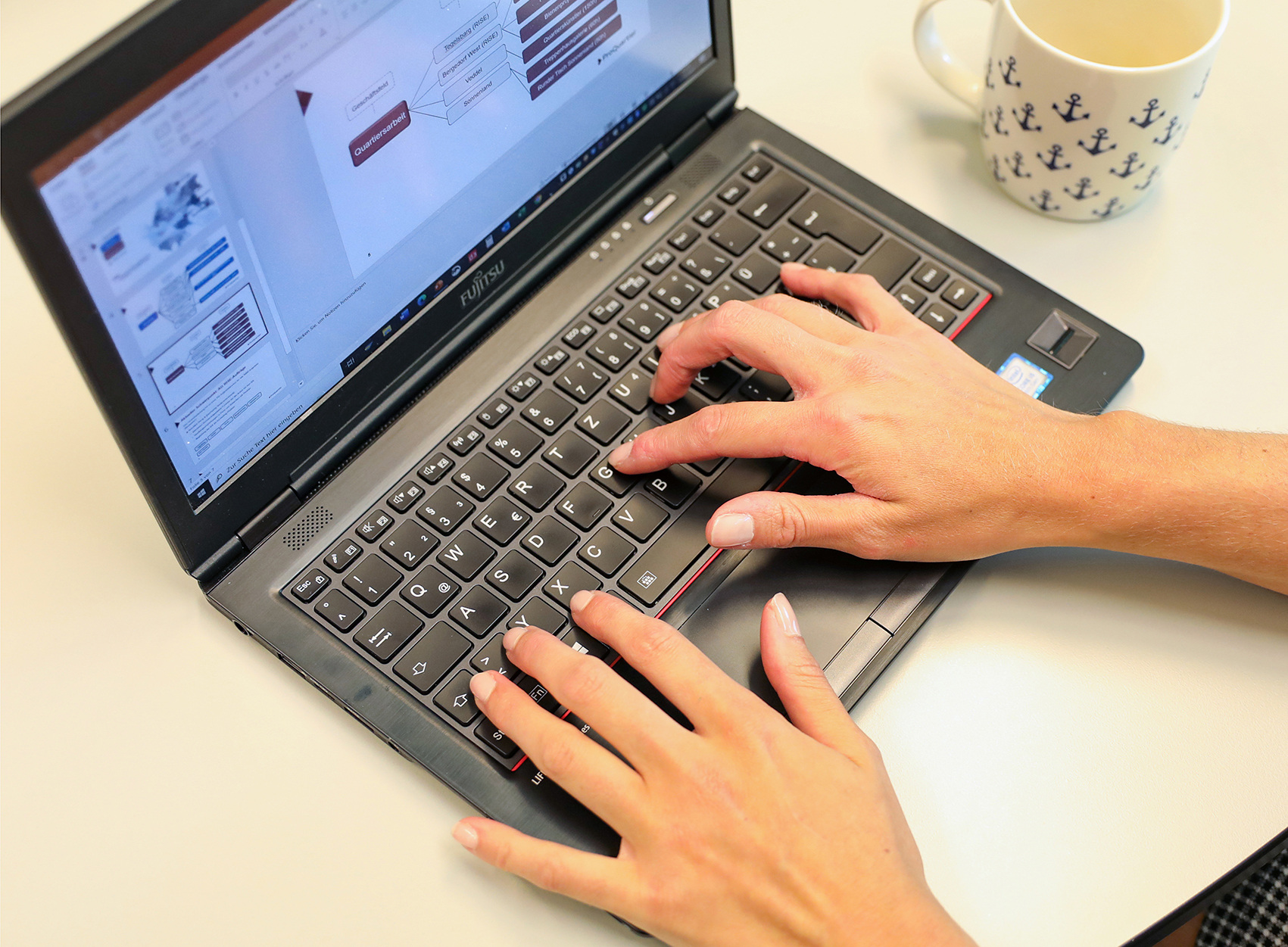 Ein aufgeklappter Laptop an dem zwei Hände auf der Tastatur tippem