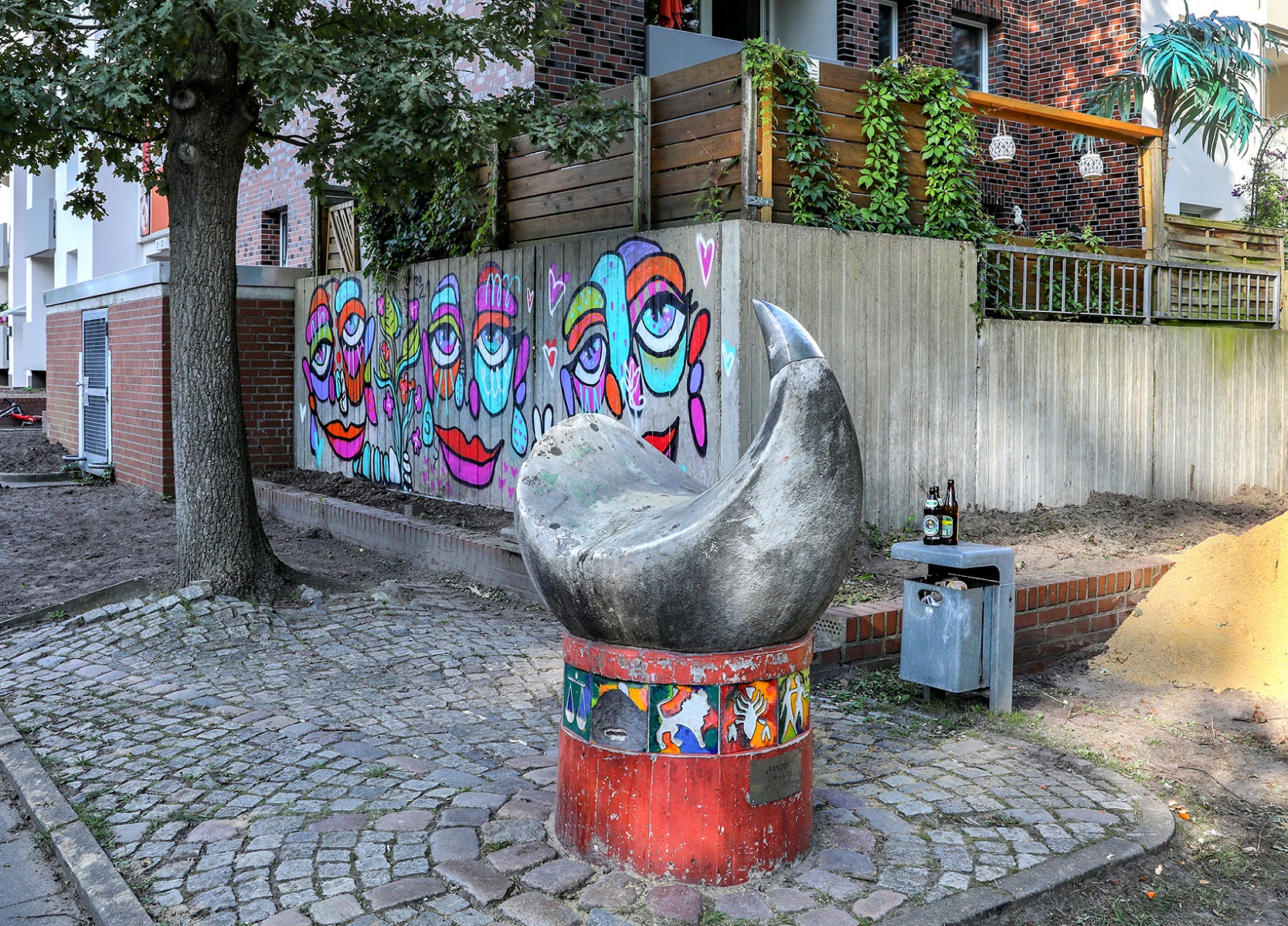 Street Art Kunstwerk installiert an einer Betonmauer, davor steht eine Stahlskulptur.