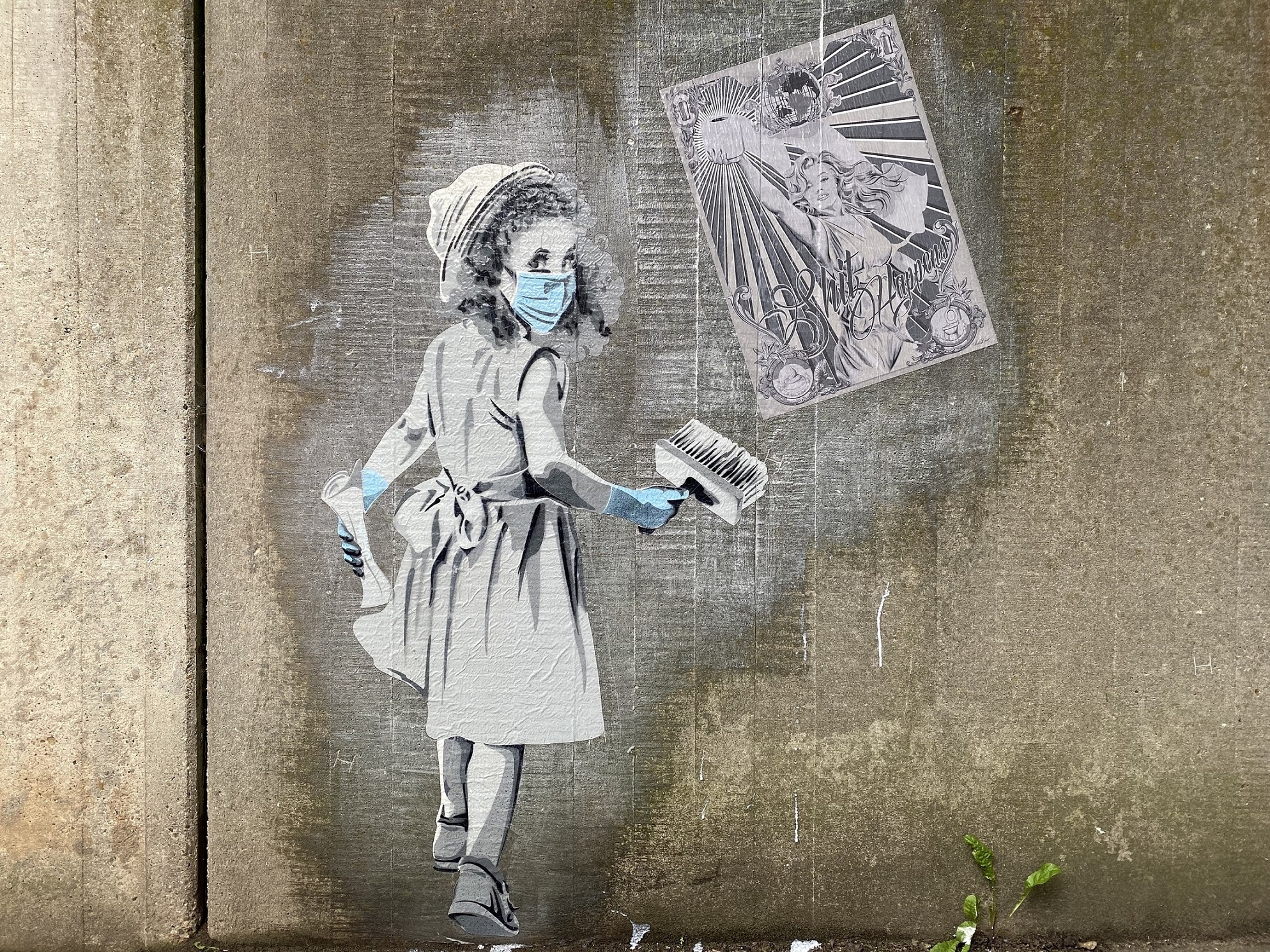Street Art Kunstwerk angebracht auf einer Betonmauer. Zu sehen ist ein in schwarz weiß Schema gehaltenes Mädchen, welches ein Plakat an eine Wand kleistert. Das Mädchen trägt akzentuiert einen hellblauen Mundschutz und hellblaue Handschuhe.