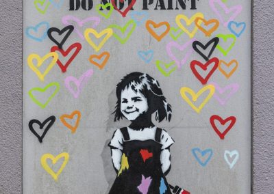 Ein Streetart Werk: Ein kleines Mädchen malt ganz viele bunte Herzen auf eine Tür auf der steht "So not paint"