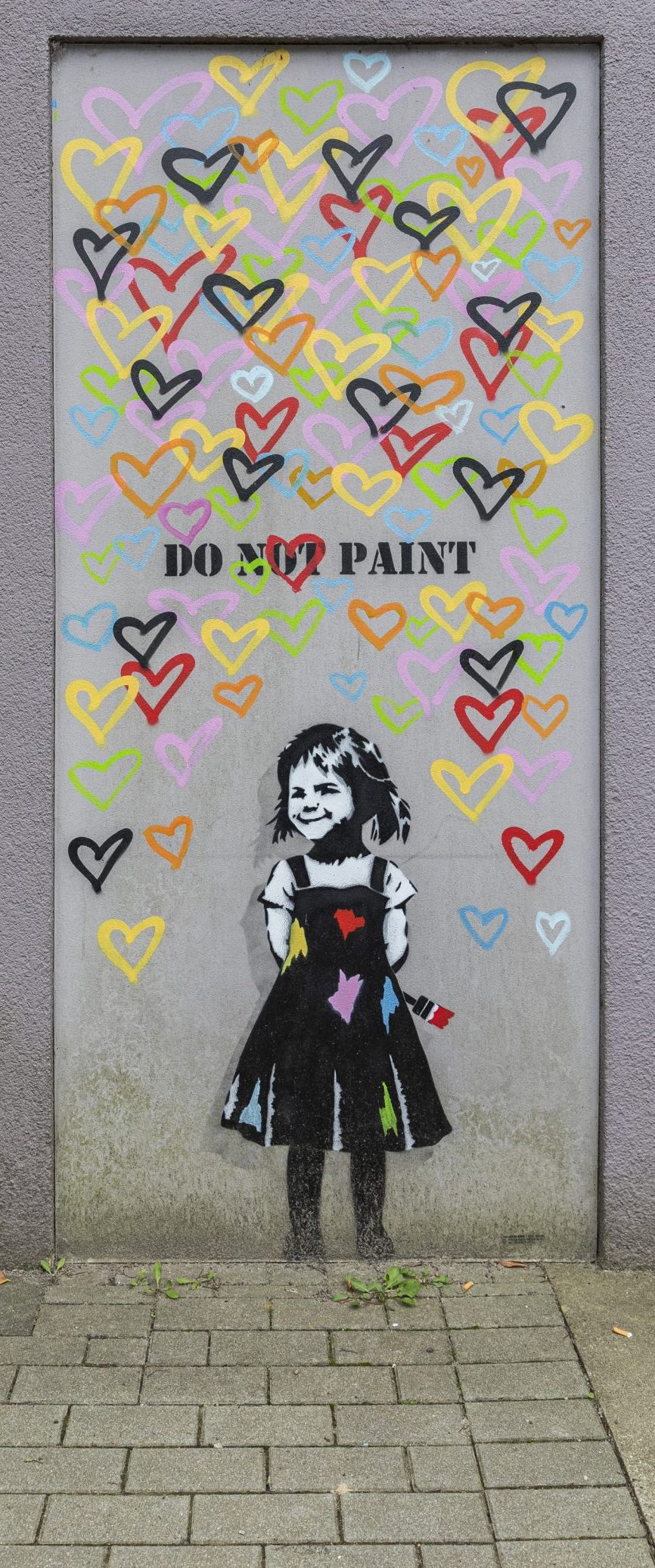 Ein Streetart Werk: Ein kleines Mädchen malt ganz viele bunte Herzen auf eine Tür auf der steht "So not paint"